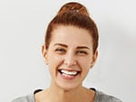 Headshot of good-looking emotional young Caucasian woman with hair knot squinting eyes while laughing out loud happy with good positive news smiling broadly showing her straight white teeth
