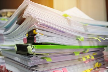 Papers with old sticky notes are piled on a desk surface.